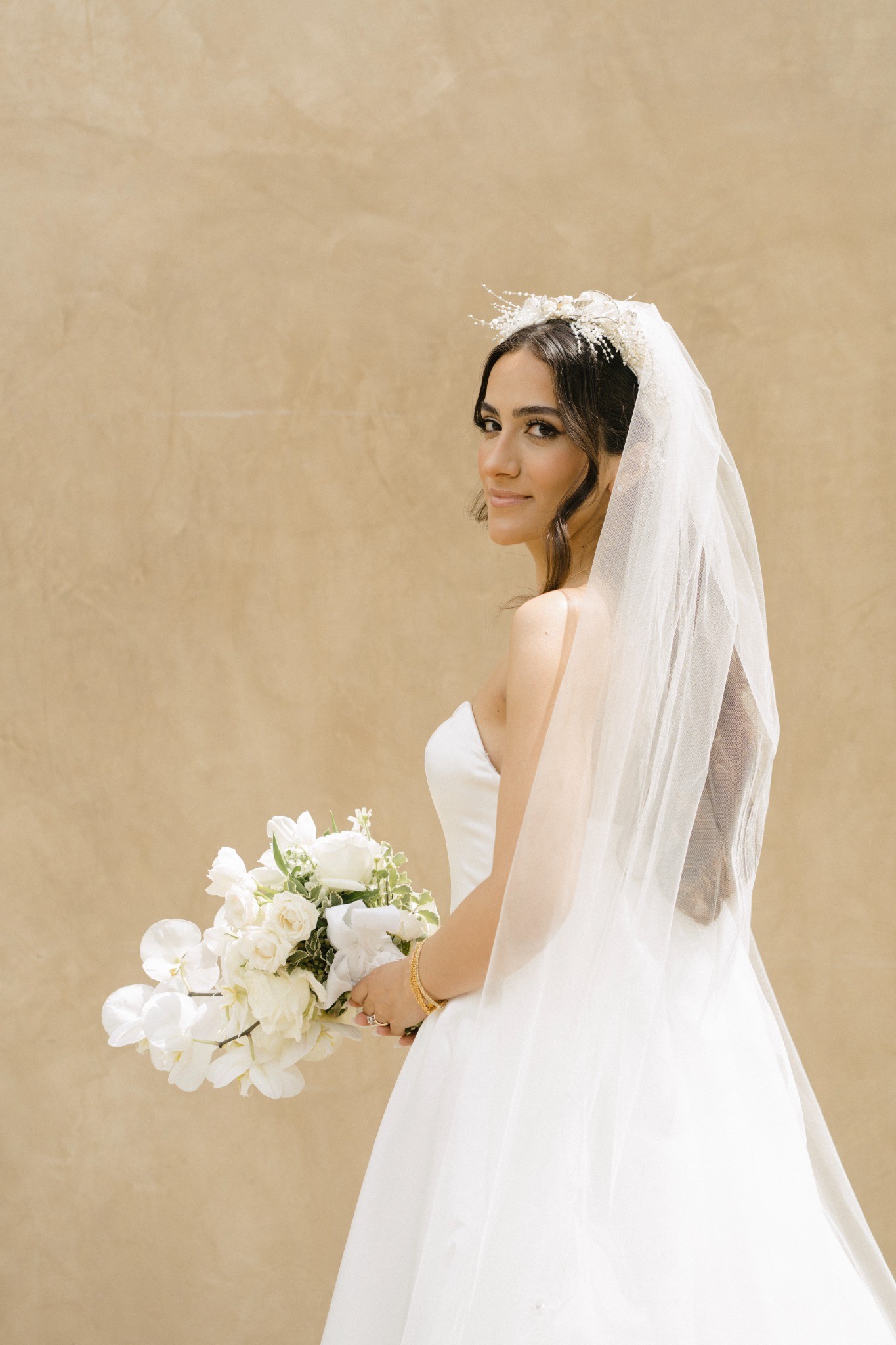 Bride holding a white bouquet against a warm stone wall